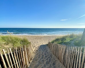 Ein sandiger Küstenweg führt zum Meer, begrenzt von Holzzaun.
