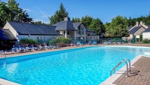 Ein Schwimmbecken mit Liegestühlen und einem Gebäude im Hintergrund.