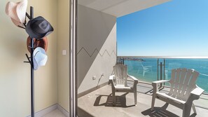 Ein Balkon mit Meerblick, zwei weiße Stühle und ein Hutfächer mit mehreren Hüten.