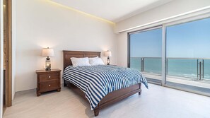 Ein Schlafzimmer mit einem großen Bett, zwei Nachttischen mit Lampen und einem Balkon mit Meerblick.