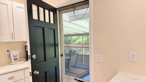 A kitchen with white cabinets, a black door, and a window with a view of the outdoors.