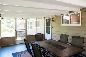 A covered patio with a table and chairs, a string of lights, and a view of the backyard.