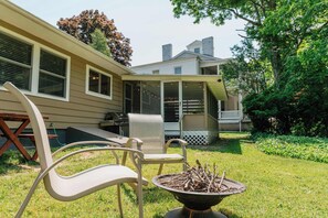 Ein Garten mit Feuerstelle, Sitzgelegenheiten im Freien und einer überdachten Terrasse.