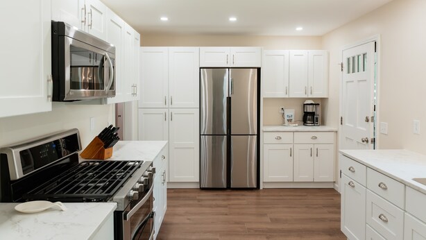 A modern kitchen with white cabinets, stainless steel appliances, and a wooden floor.