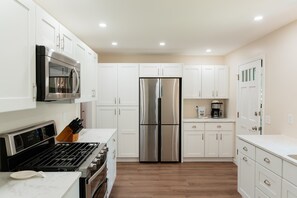 A modern kitchen with white cabinets, stainless steel appliances, and a wooden floor.