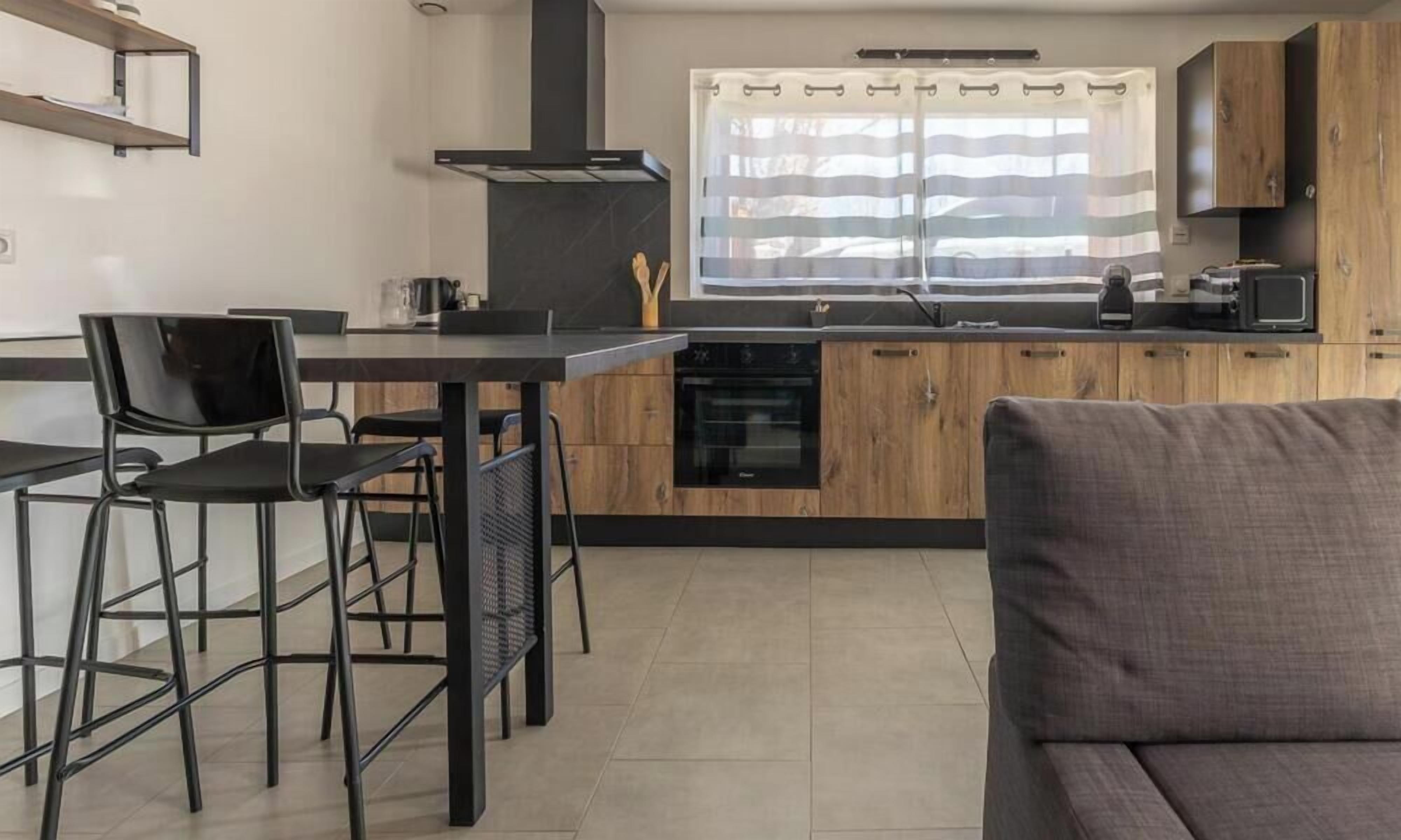 A compact kitchen with a dining area, wooden cabinets, a built-in oven, and a window with curtains.