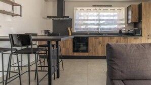 Uma cozinha compacta com área de jantar, armários de madeira, forno embutido e uma janela com cortinas.