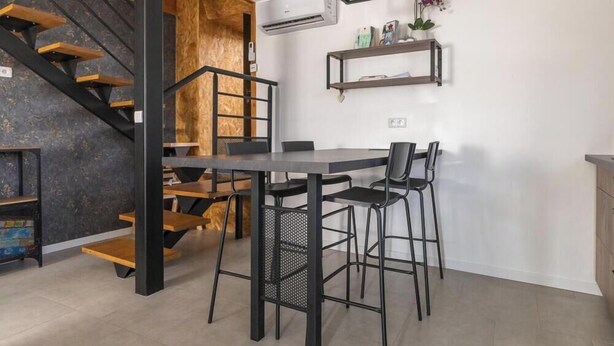 Uma cozinha moderna com escada de madeira, mesa de jantar com cadeiras e estantes embutidas.