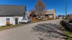 Uma estrada rural com casas, um carro estacionado e um céu azul claro.