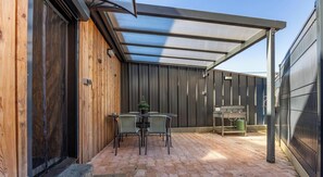 Eine überdachte Terrasse mit Tisch, Stühlen, einem Grill und einer Holzwand.