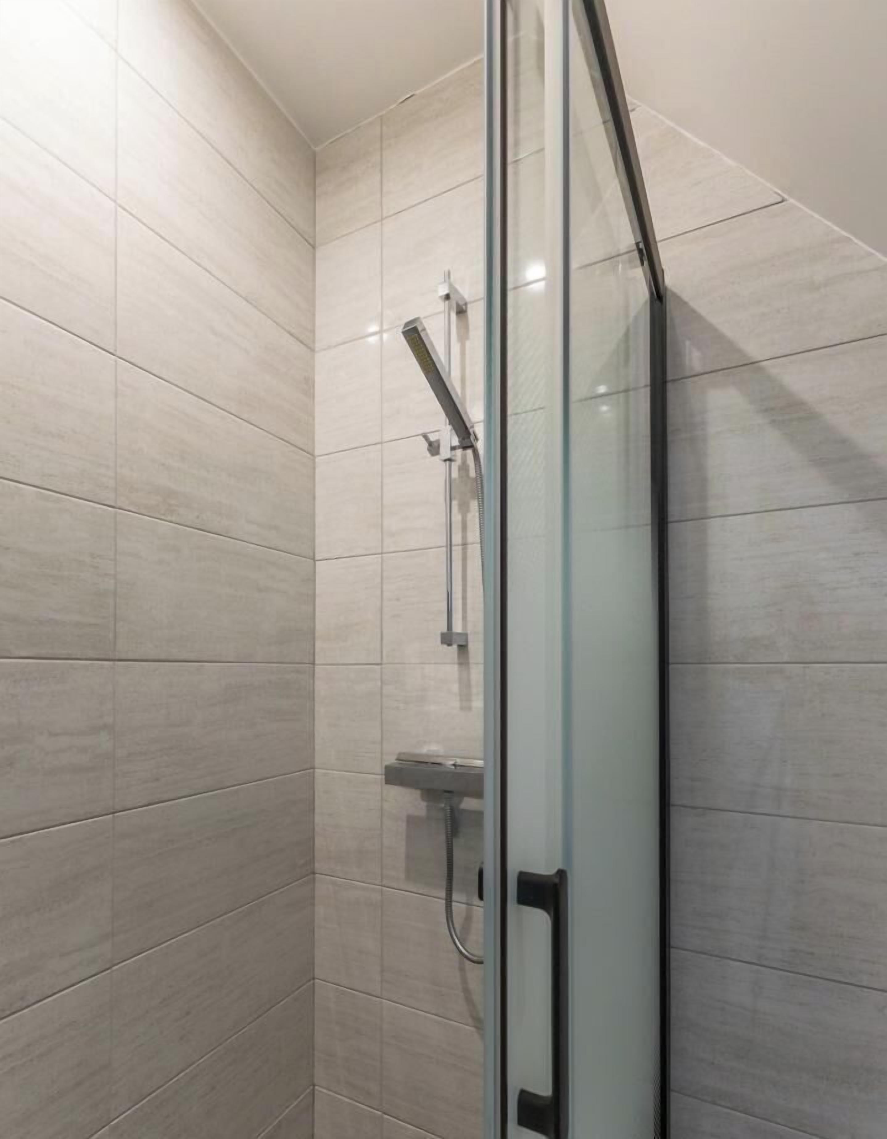 Una ducha con mampara de vidrio, paredes de azulejos y cabezal de ducha de mano.