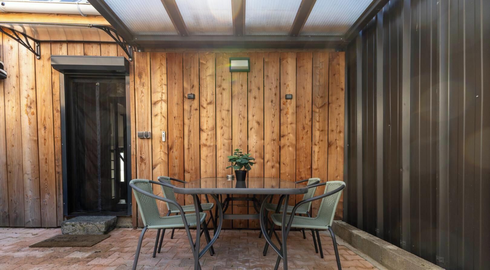 Una habitación con paneles de madera, una mesa de vidrio y sillas, una planta en maceta y una puerta.