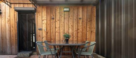 Una habitación con paneles de madera, una mesa de vidrio y sillas, una planta en maceta y una puerta.