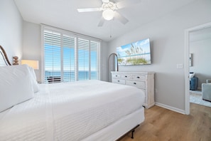 Ein Schlafzimmer mit Bett, Deckenventilator, Fenster mit Jalousien, Kommode und einem Bild an der Wand.