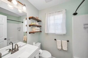 A bathroom with a sink, mirror, towel racks, and a shower area. - Island Home. 15 mins to Tybee Beach & Downtown., Sleeps 10 (Savannah)