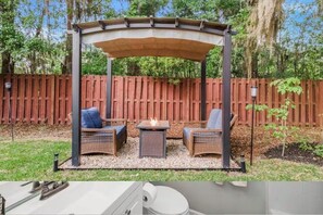 A covered patio area with wicker furniture and a fire feature. - Island Home. 15 mins to Tybee Beach & Downtown., Sleeps 10 (Savannah)