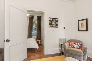A hotel room with a bed, a chair with a colorful pillow, a small table, and a wall with framed pictures. - Savannah Home, Walkable to Forsyth, Historic, Dogs OK, Free Parking for 2 Cars (Savannah)