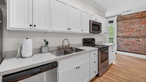 A modern kitchen with white cabinets, stainless steel appliances, and a brick wall. - Harbor View Suite C in Historic Georgetown (Georgetown)