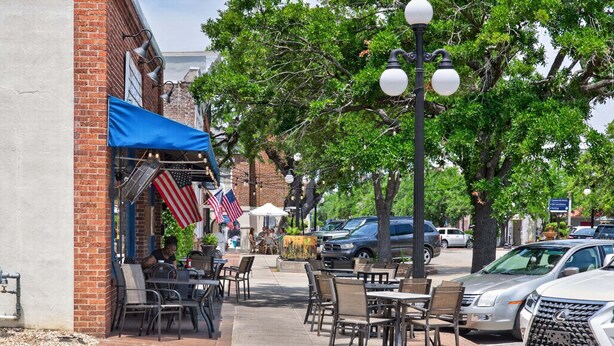 A sidewalk cafe with outdoor seating, American flags, and parked cars. - Harbor View Suite C in Historic Georgetown (Georgetown)