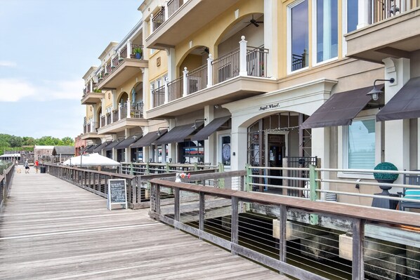A waterfront promenade with a wooden walkway, outdoor seating, and a row of buildings with balconies.