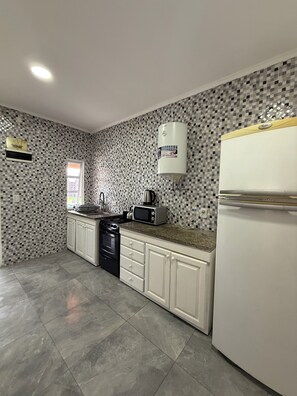 A kitchen with a tiled backsplash, a stove, a microwave, a refrigerator, and a water heater.