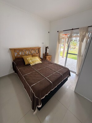 Un dormitorio con cama, mesita de noche, lámpara y vistas al exterior.
