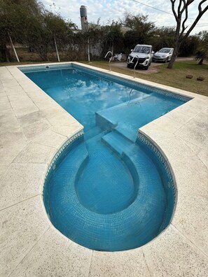 Una piscina rectangular de diseño único, rodeada por un solárium empedrado.