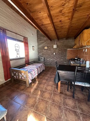 A rustic room with a bed, a dining table, and a kitchen area.