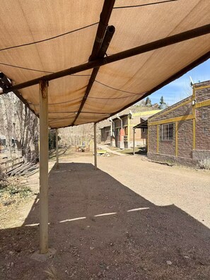 A covered outdoor area with a dirt ground, metal poles, and a brick building in the background.