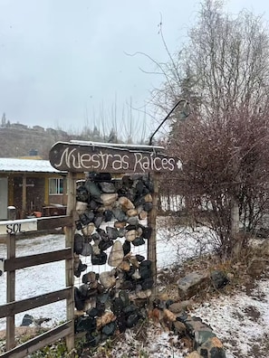 Un letrero de madera rústico con el texto 'Miesas Raices' y un muro de piedra con varias rocas.