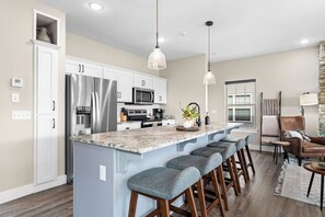 Una cocina moderna con una isla central, taburetes de bar, electrodomésticos de acero inoxidable e iluminación colgante.