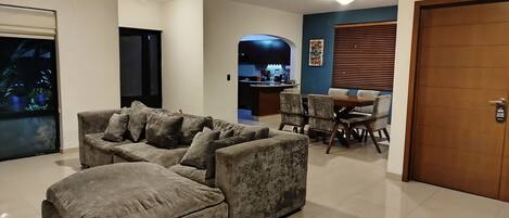 A living room with a sectional sofa, a dining area with a table and chairs, and a kitchen in the background.
