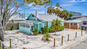 A small, single-story house with a light blue exterior, a covered porch, and a small garden with palm trees and shrubs. - 2BR & Beach Gear | Walk to Treasure Island Beach (Treasure Island)