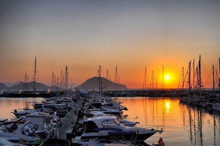 A marina with boats docked, a sunset in the background, and a distant mountain.. MY MARİN HOTEL