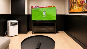 Ein modernes Wohnzimmer mit einem wandmontierten Flachbildfernseher, einer schwarzen Unterhaltungseinheit darunter, einem runden Couchtisch mit Fernbedienung und einem beigefarbenen Sofa.