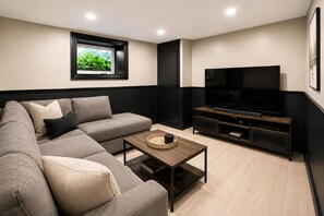 Una sala moderna con un sofá seccional, una mesa de centro, un televisor sobre un mueble de madera y una ventana con follaje.