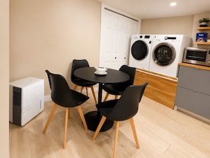 Cozinha compacta com área de jantar, incluindo mesa e cadeiras, máquina de lavar, micro-ondas e uma pequena geladeira.