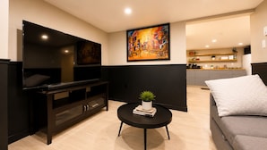 Ein modernes Wohnzimmer mit Fernseher, einem Gemälde, einem kleinen Tisch mit Pflanze und einem grauen Sofa.