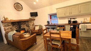 Ein gemütliches Wohnzimmer mit Kamin, ein Essbereich mit Holzmöbeln sowie eine Küche mit hellen Schränken und modernen Geräten.