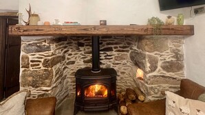 Ein Kamin aus Stein mit einer modernen Uhr darüber, ein Flachbildfernseher an der Wand und eine gemütliche Sitzecke mit braunen Kissen.