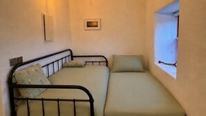 Ein kleines Zimmer mit zwei Betten, einem Fenster, einer Lampe und einem Bild an der Wand.