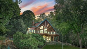 A large, two-story house with a prominent gabled roof, surrounded by lush greenery and a well-maintained lawn. - Mi Casa, Su Casa | Fire Pit | Dock | Game Rom | Sleeps 14 (Sherrills Ford)