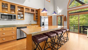 A modern kitchen with wooden cabinets, stainless steel appliances, and a large island with bar stools. - Mi Casa, Su Casa | Fire Pit | Dock | Game Rom | Sleeps 14 (Sherrills Ford)