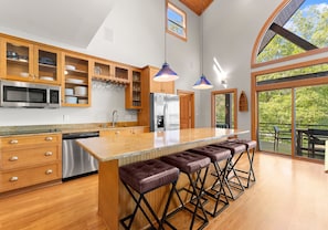 A modern kitchen with wooden cabinets, stainless steel appliances, and a large island with bar stools. - Mi Casa, Su Casa | Fire Pit | Dock | Game Rom | Sleeps 14 (Sherrills Ford)