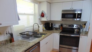 Una cocina con alacenas blancas, horno de acero inoxidable, microondas, lavaplatos y escurreplatos.