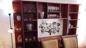 Un comedor con mesa y sillas de madera, rodeado de estanterías de madera con cristalería y objetos decorativos.