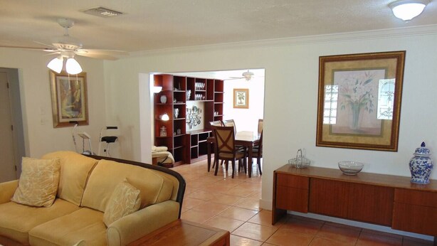 Una sala de estar con un sofá, una mesa de centro de madera, una zona de comedor con sillas y una mesa, una estantería y un cuadro enmarcado en la pared.