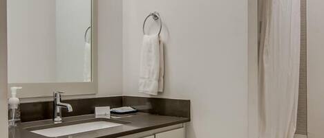 A modern bathroom with a large mirror, a sink, a towel rack, and a shower curtain.
