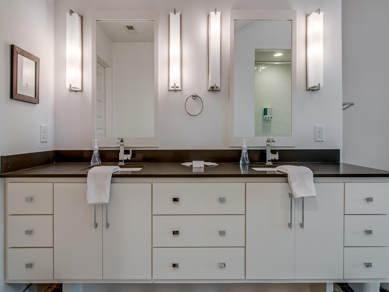 A modern bathroom with two sinks, a large mirror, and a towel rack.