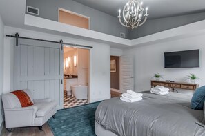 Ein Schlafzimmer mit einem großen Bett, einem Sessel, einem Fernseher und einem durch eine geöffnete Tür sichtbaren Badezimmer.